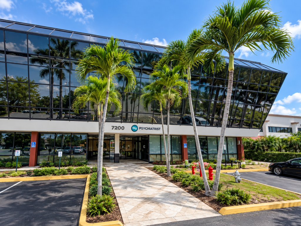 A modern glass-fronted building with palm trees and a sign reading PSYCHIATRIST above the entrance, reflecting the professional atmosphere of psychiatrists in Boca Raton, FL. The address 7200 is visible, and there are parking spaces and fire hydrants in front.