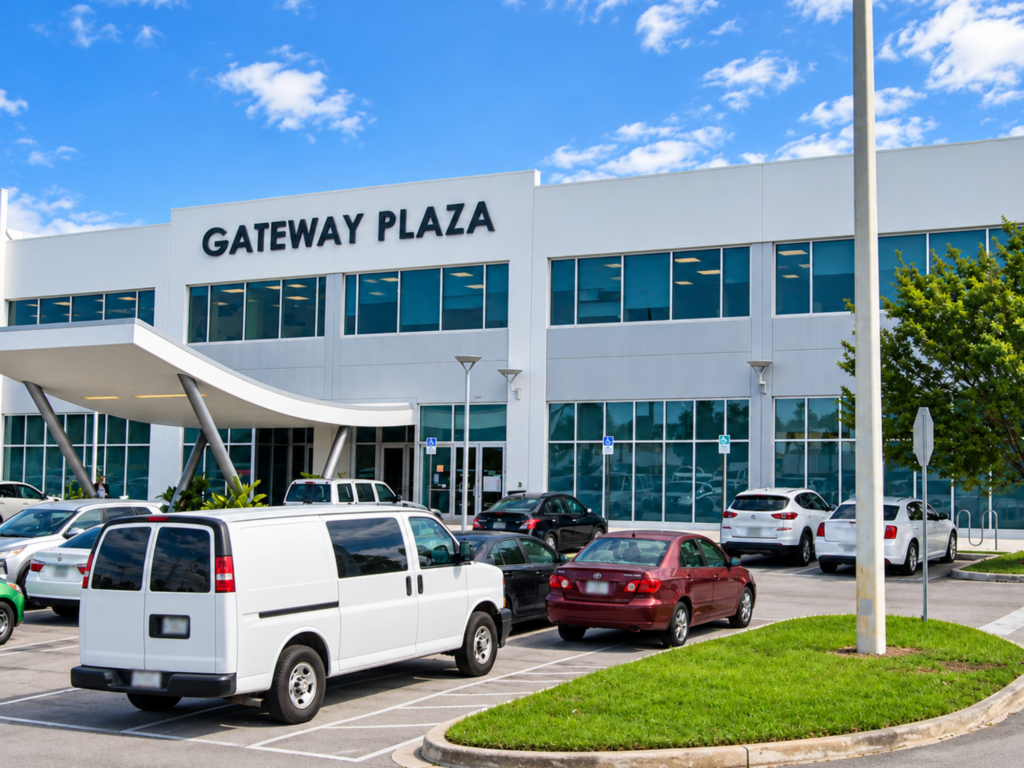 A two-story white office building labeled Gateway Plaza, with parked cars in front, a covered entrance, and a clear blue sky overhead—an inviting location for anyone seeking a psychiatrist in Doral, FL.