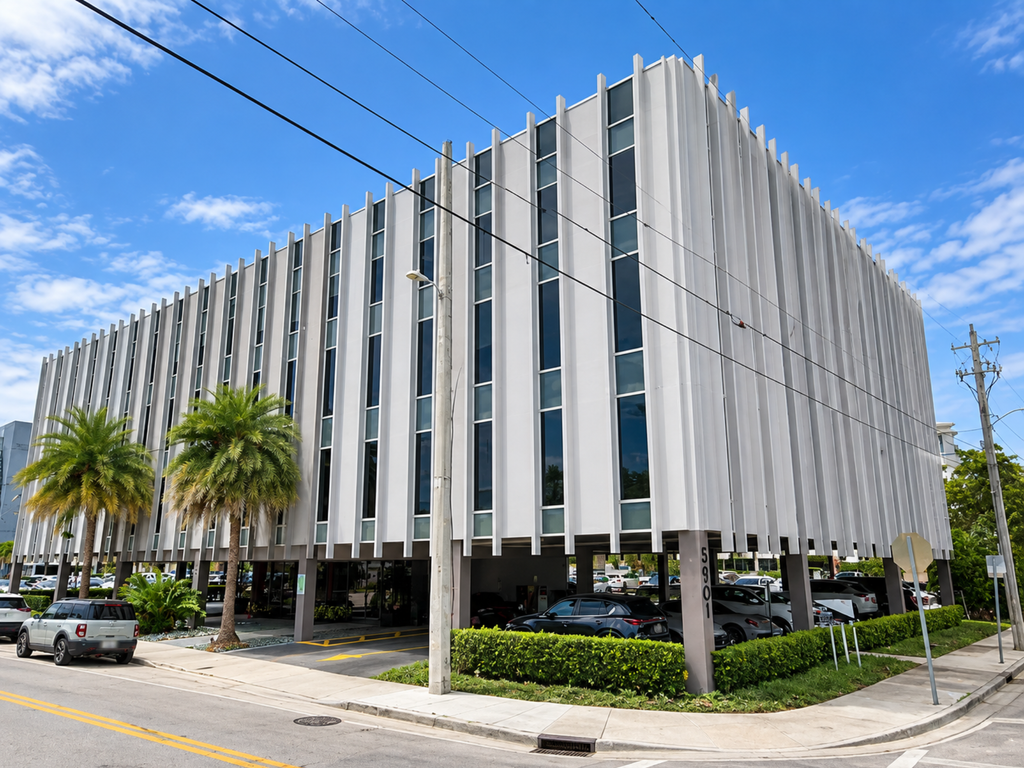 A modern, white multi-story office building on stilts with vertical fins, palm trees in front, cars parked underneath, and a bright blue sky above—an ideal location for a psychiatrist in Miami seeking an inspiring workspace.