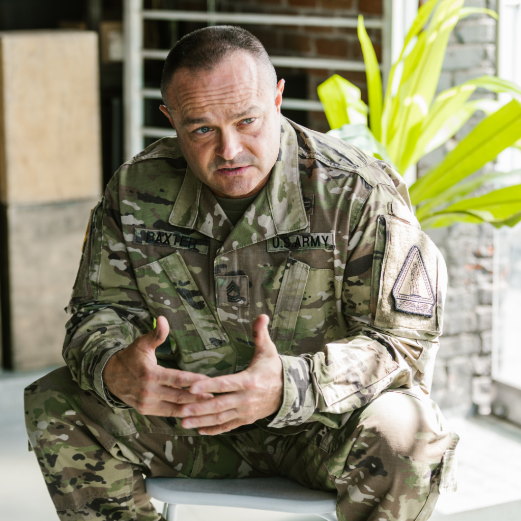 A US Army soldier in camouflage uniform sitting and speaking with his hands gesturing during a consultation at a PTSD treatment center in Florida.